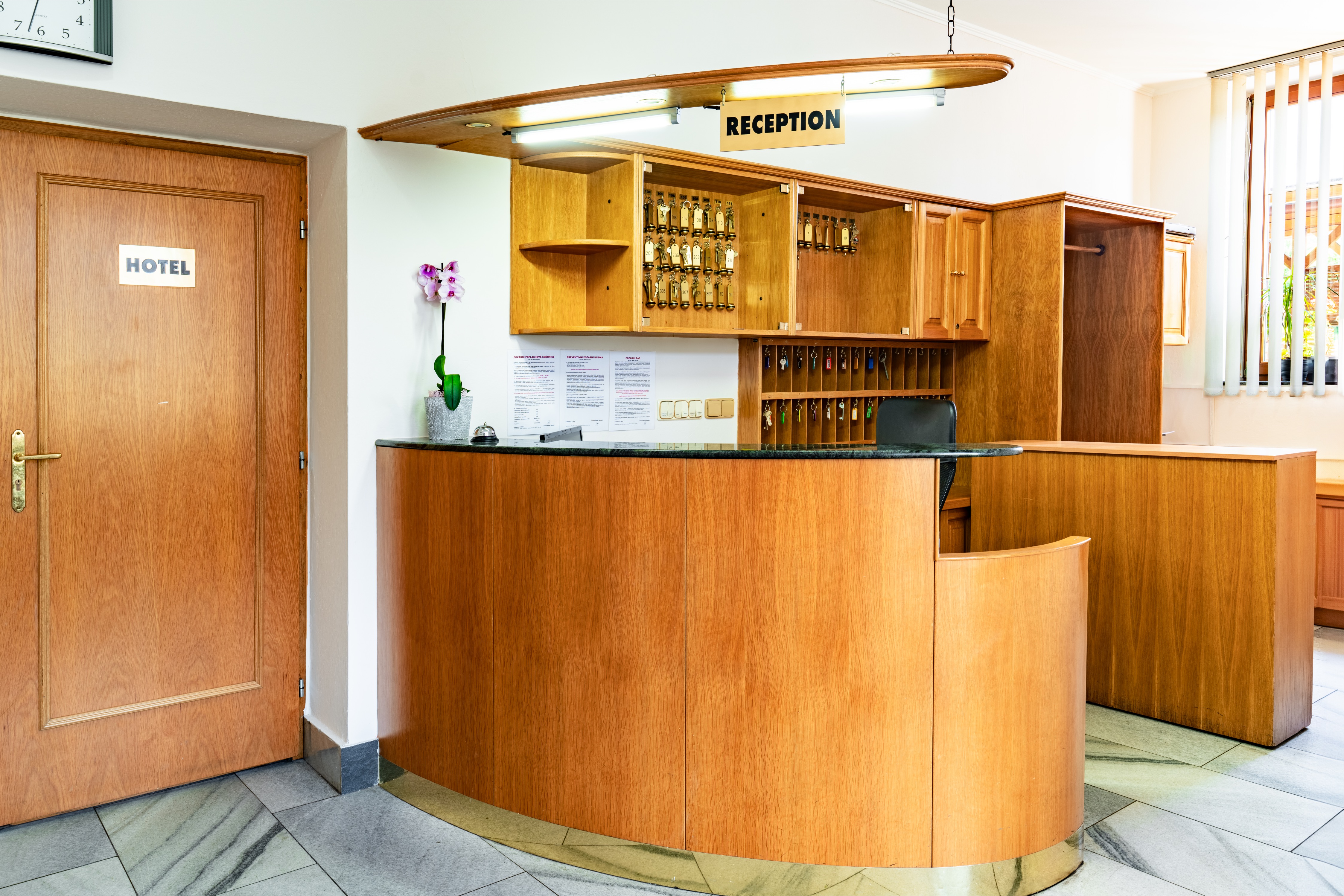 Hotel reception desk with wooden cabinetry, key hooks, and an orchid plant beside a door labeled HOTEL.