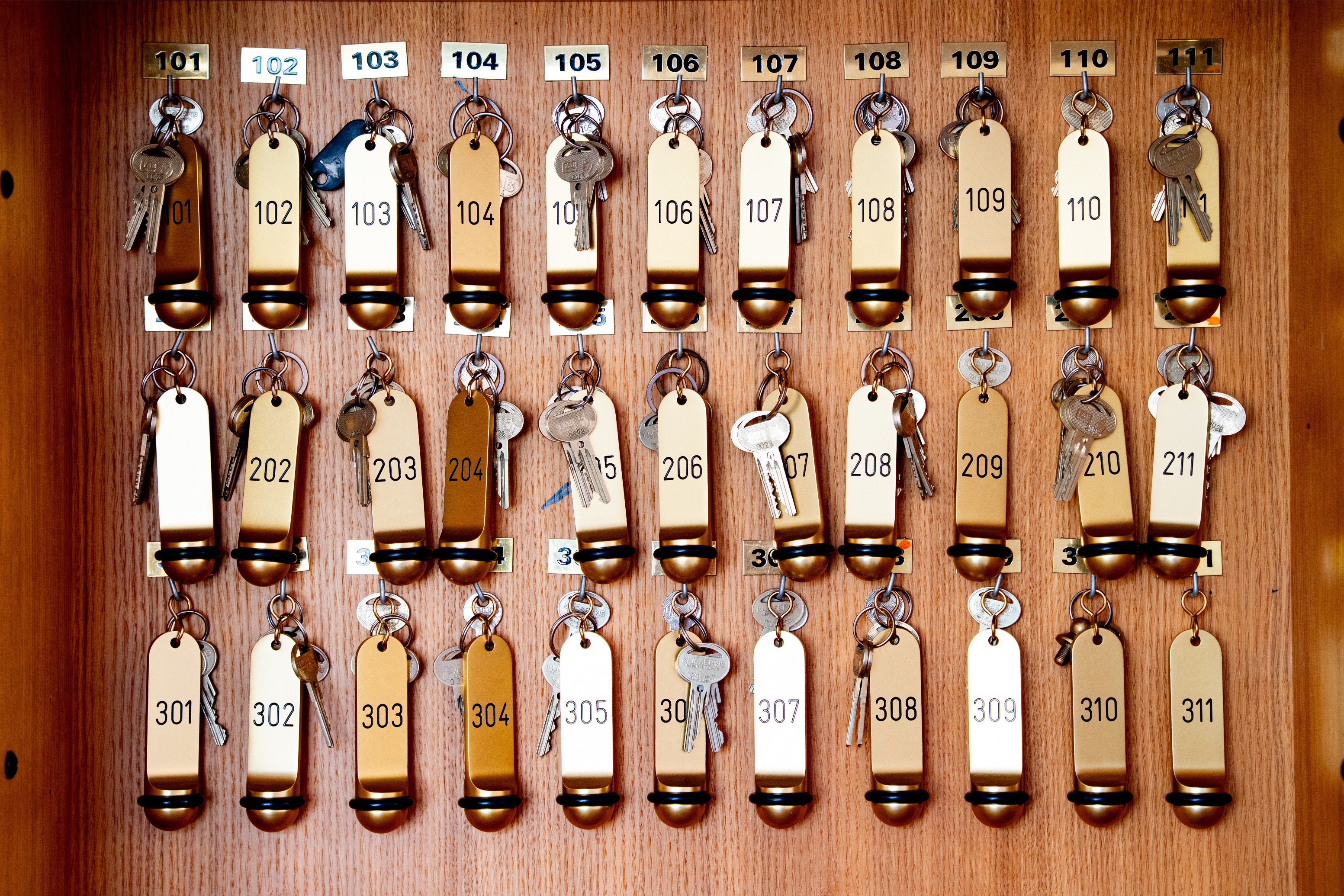 Wooden key rack with rows of room keys labeled 101 to 111, 202 to 211, and 301 to 311.